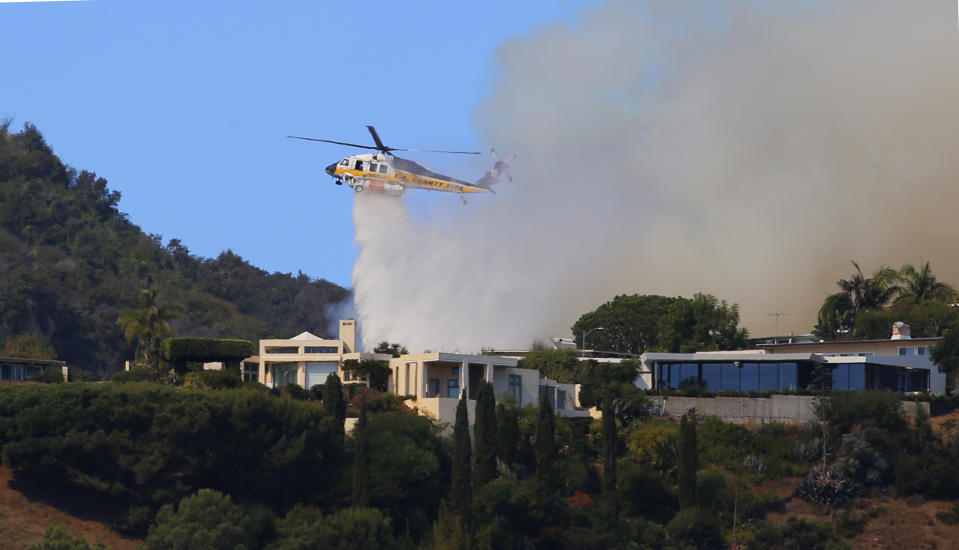 A helicopter makes a water drop as flames threaten homes on a ridgeline as a wildfire threatens homes in the Pacific Palisades area of Los Angeles, Monday, Oct. 21, 2019. (AP Photo/Reed Saxon)