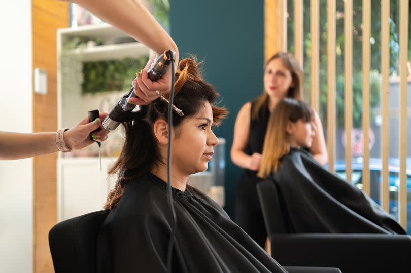 Selective focus on the hands of a hairdresser using an electric curling iron with a client