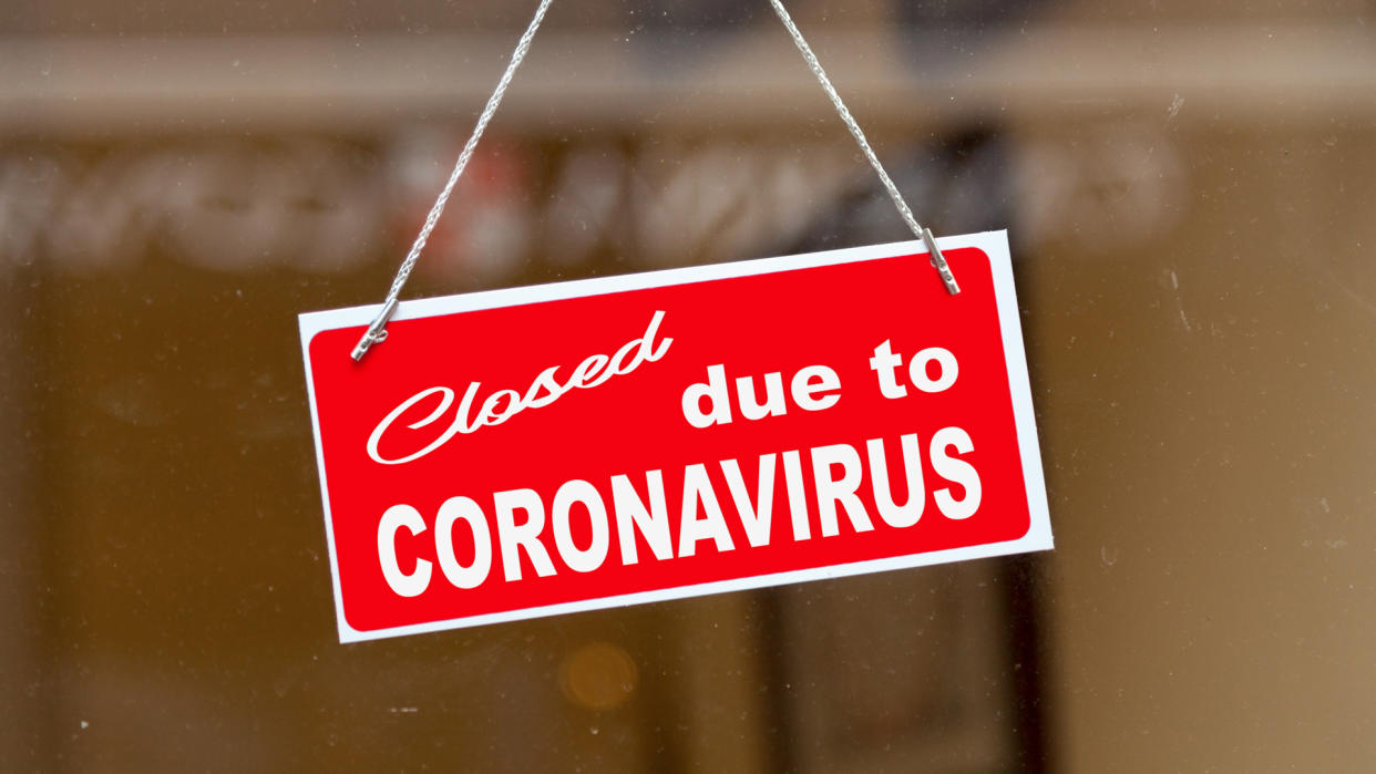 Red sign hanging at the glass door of a shop saying "Closed due to coronavirus".