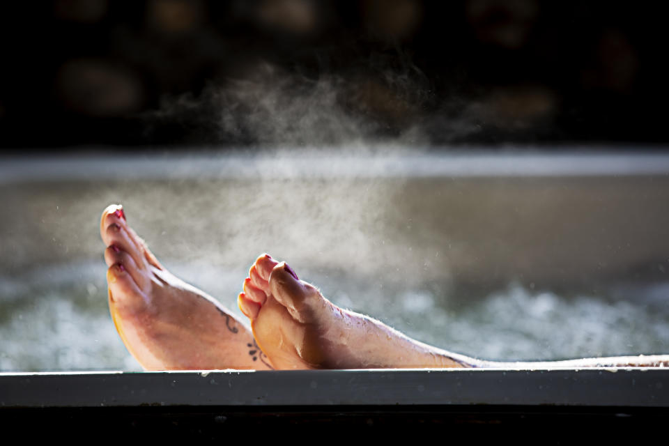 Woman holds her feet up while in a hot tub with steam