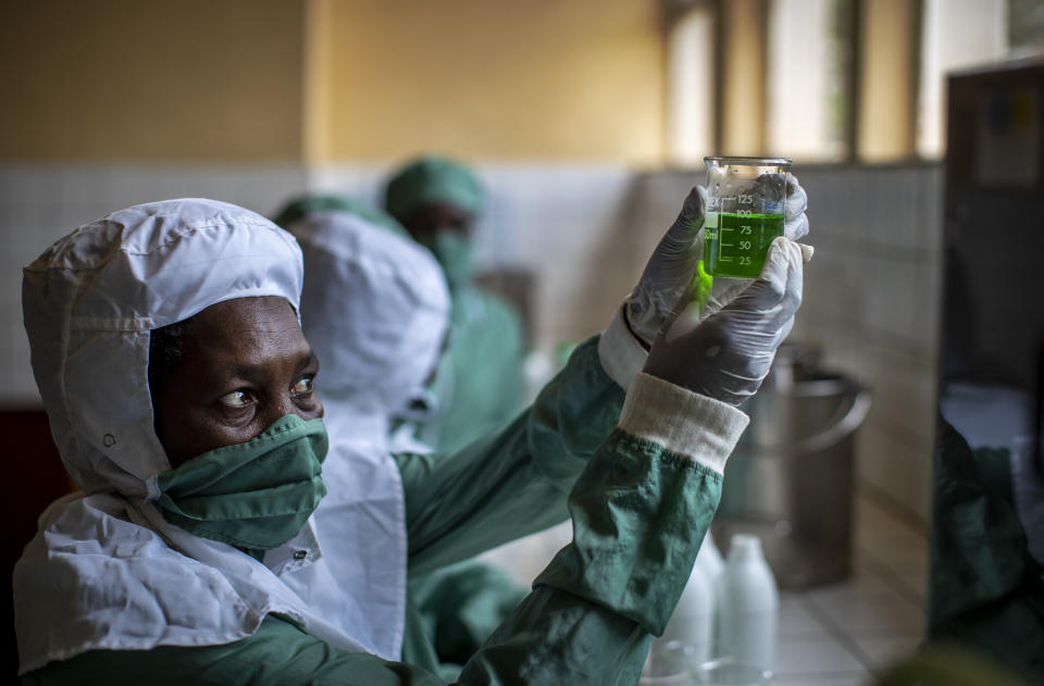 In this photo taken Thursday, Nov. 7, 2019, workers wearing protective clothing to protect from the effects of the drug and to prevent contamination, make liquid morphine from powder which is dyed green as a color-code to indicate the strength, at the Pharmaceutical Laboratory of Rwanda in Butare, Rwanda. While people in rich countries are dying from overuse of prescription painkillers, people in Rwanda and other poor countries are suffering from a lack of them, but Rwanda has come up with a solution to its pain crisis - it's morphine, which costs just pennies to produce and is delivered to households across the country by public health workers. (AP Photo/Ben Curtis)