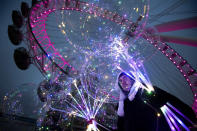 A man holds illuminated balloons, standing in front of the London Eye tourist sightseeing wheel in London, Monday Dec. 28, 2020. Millions more people moved to harsher coronavirus restrictions as the new tier changes came into force over much of England. (Victoria Jones/PA via AP)