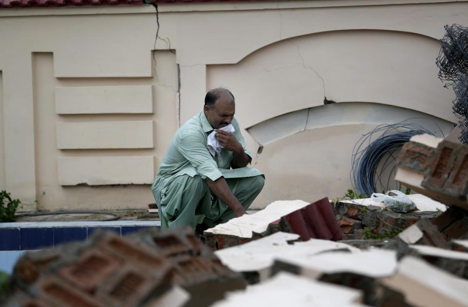 A man who lost his sister mourns for her next to a damaged wall of his house caused by a powerful earthquake at Sahang Kikri village near Mirpur, northeastern Pakistan, Wednesday, Sept. 25, 2019. Mourners were burying their dear ones in Pakistan-held Kashmir where a powerful earthquake struck a day before. (AP Photo/Anjum Naveed)