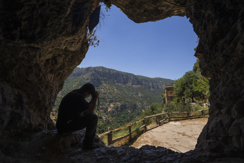 Lebanese priest Hani Tawk prays in a cave by the Qannoubine Monastery, hidden deep in the Kadisha Valley, a holy site for Lebanon's Maronite Christians, in the northeast mountain town of Bcharre, Lebanon, Saturday, July 22, 2023. For Lebanon's Christians, the cedars are sacred, these tough evergreen trees that survive the mountain's harsh snowy winters. They point out with pride that Lebanon's cedars are mentioned 103 times in the Bible. (AP Photo/Hassan Ammar)