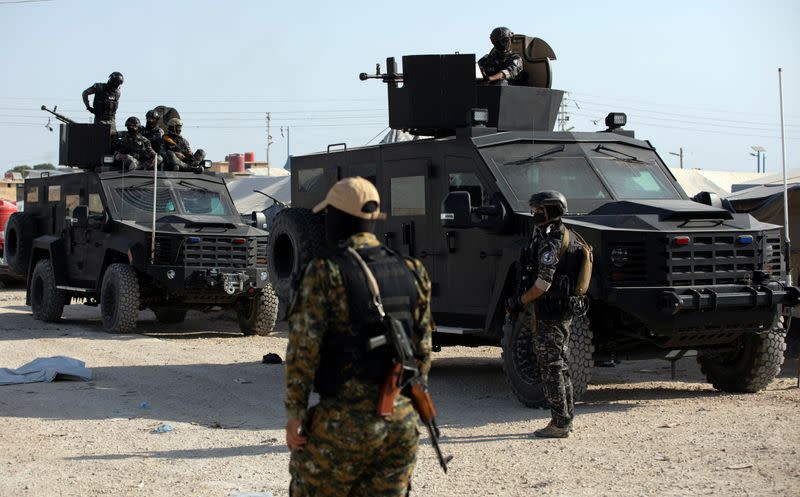 An SDF fighter stands near Kurdish internal security special forces during a security operation in al-Hol camp