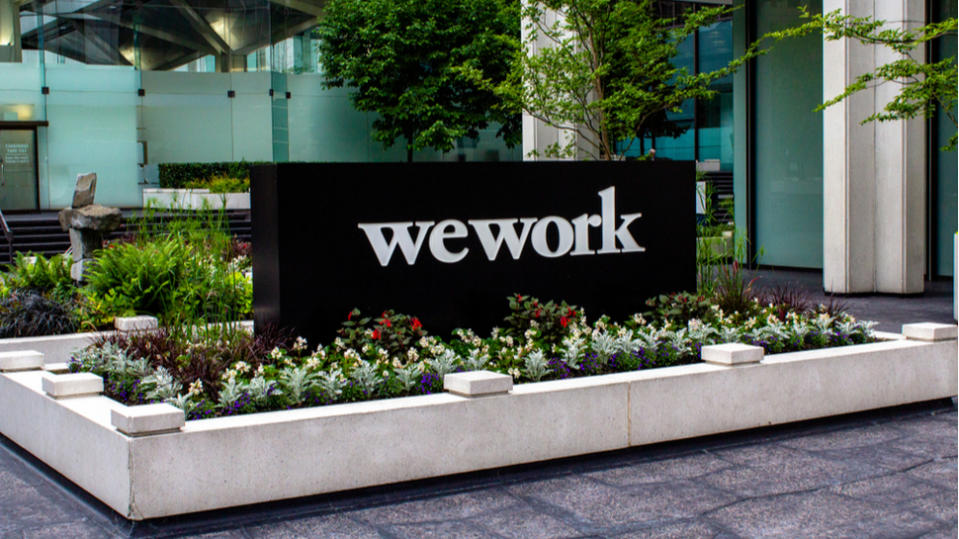 The black and white WeWork logo on a sign surrounded by a bed of flowers.