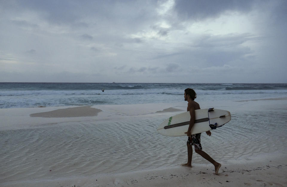 A surfer carries his board on Playa Gaviota Azul as Tropical Storm Zeta approaches Cancun, Mexico, Monday, Oct. 26, 2020. A strengthening Tropical Storm Zeta is expected to become a hurricane Monday as it heads toward the eastern end of Mexico's resort-dotted Yucatan Peninsula and then likely move on for a possible landfall on the central U.S. Gulf Coast at midweek. (AP Photo/Victor Ruiz Garcia)