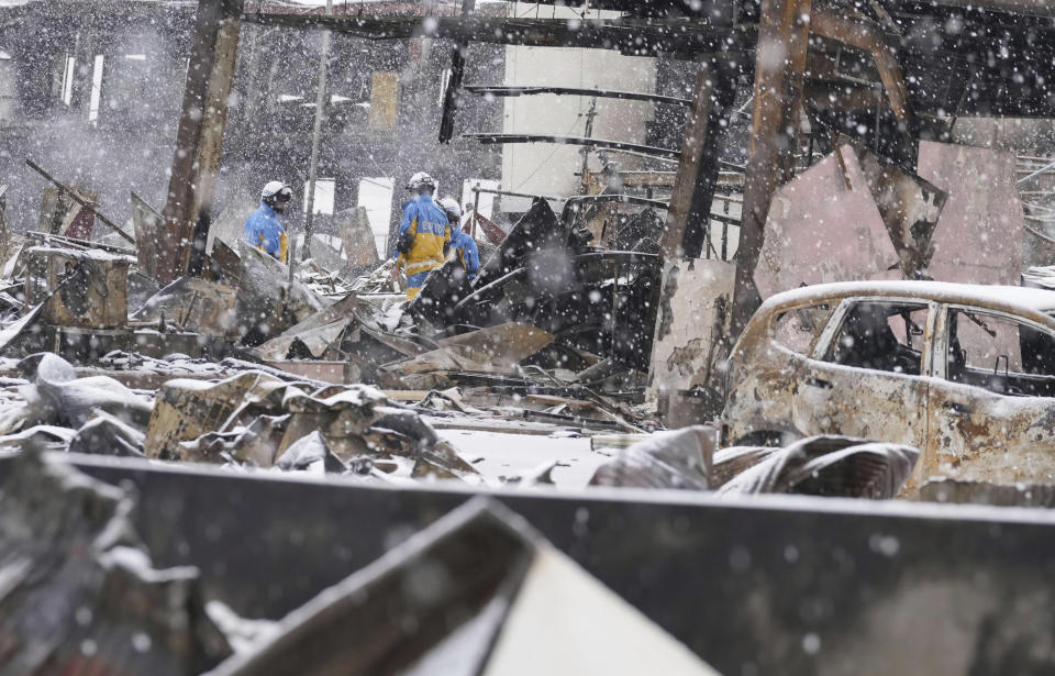 Snow falls as police officers continue a search operation around a burnt market in Wajima, Ishikawa prefecture, Japan Sunday, Jan. 7, 2024. A major earthquake slammed western Japan on Jan. 1, killing scores of people, toppling buildings and setting off landslides. (Kyodo News via AP)