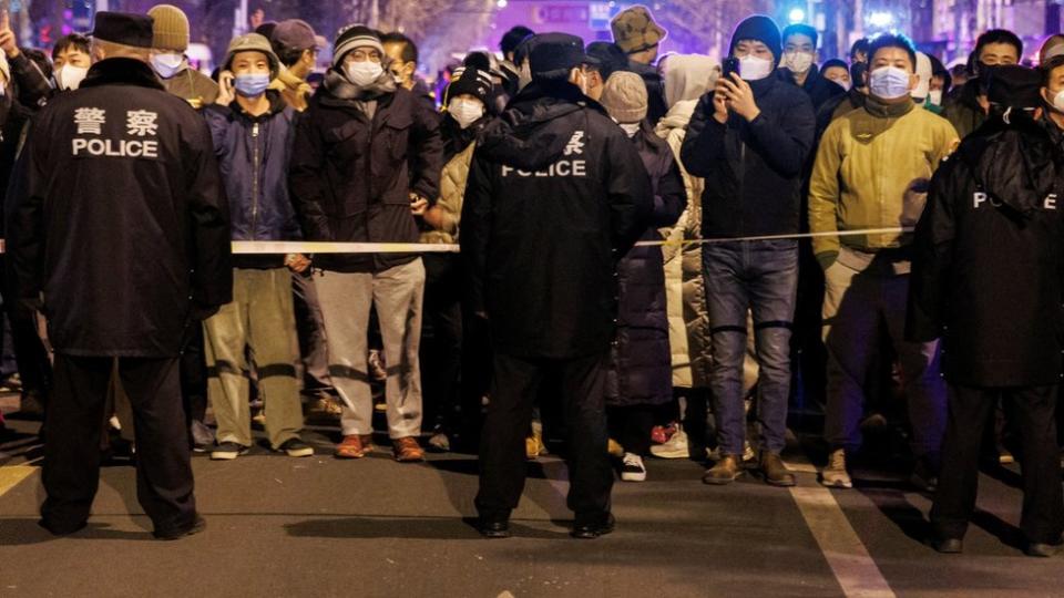 People stand behind a police cordon as they watch a protest over coronavirus disease (COVID-19) restrictions, following a commemoration of the victims of a fire in Urumqi, as outbreaks of COVID-19 continue, in Beijing, China, November 27, 2022.