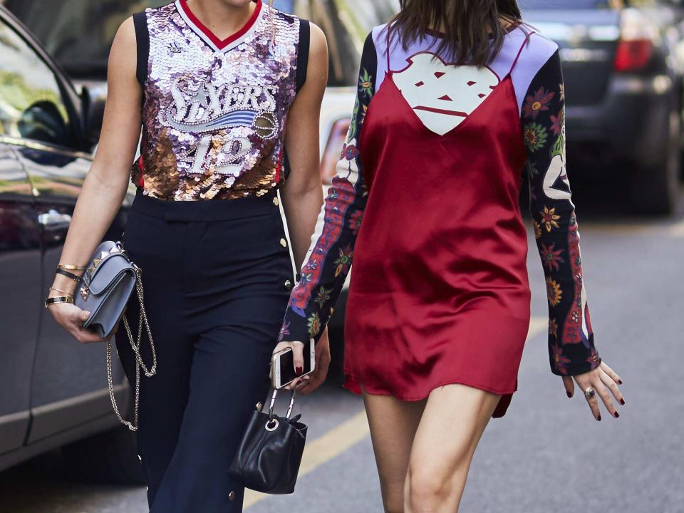 two woman in trendy, shiny outfits talking and walking down a street