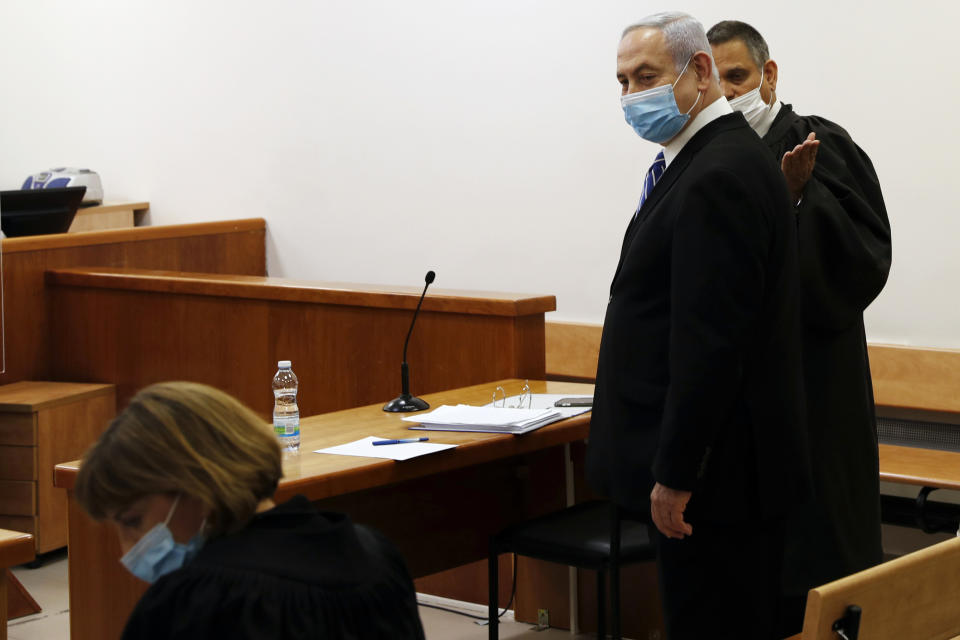 Israeli Prime Minister Benjamin Netanyahu, wearing a face mask in line with public health restrictions due to the coronavirus pandemic, stands inside the court room as his corruption trial opens at the Jerusalem District Court, Sunday, May 24, 2020. He is the country’s first sitting prime minister ever to go on trial, facing charges of fraud, breach of trust, and accepting bribes in a series of corruption cases stemming from ties to wealthy friends. (Ronen Zvulun/ Pool Photo via AP)