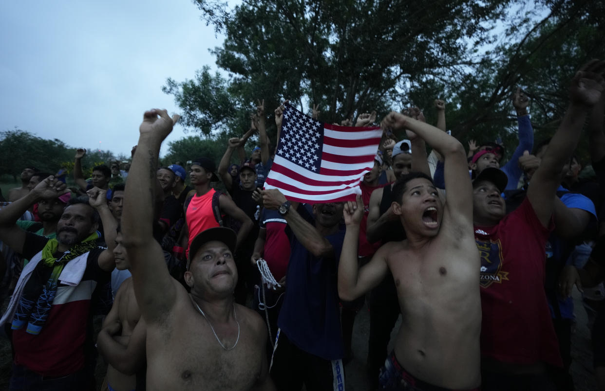 Venezuelan migrants wave a U.S. flag at a television helicopter that flew over the Rio Grande, in Matamoros, Mexico, Friday, May 12, 2023, a day after pandemic-related asylum restrictions called Title 42 were lifted. (AP Photo/Fernando Llano)