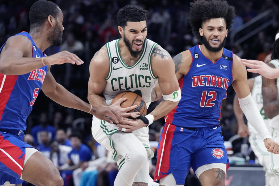 Boston Celtics forward Jayson Tatum (0) drives through Detroit Pistons guard Alec Burks, left, and forward Isaiah Livers (12), right, during the first half of an NBA basketball game, Monday, Feb. 6, 2023, in Detroit. (AP Photo/Carlos Osorio)