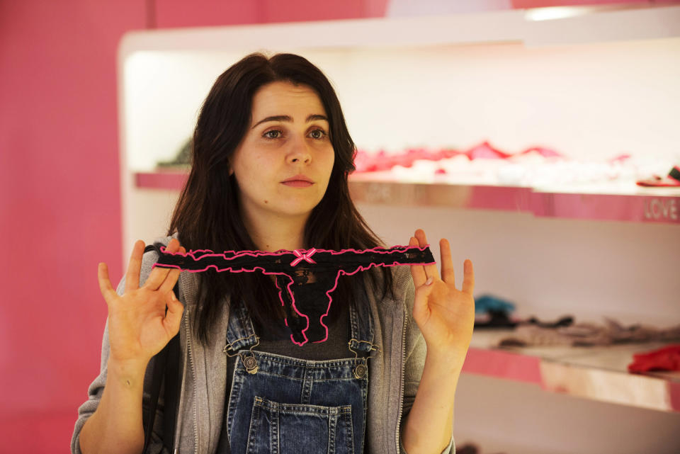 A woman holding up frilly underwear, looking confused