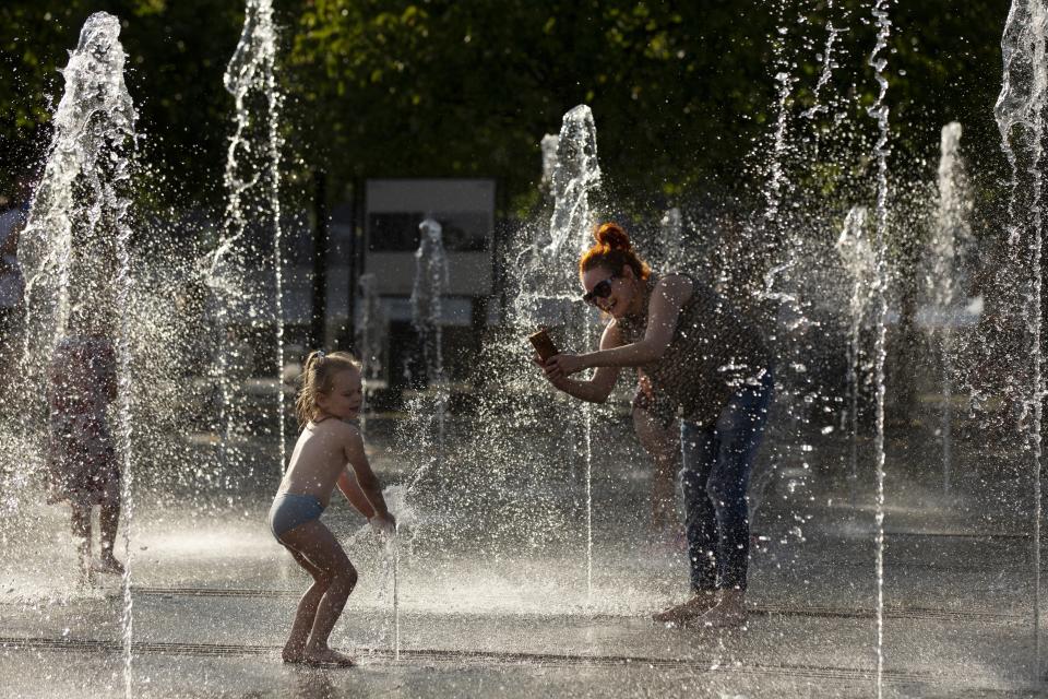 A woman takes a photo as her child plays in a fountain at a park in Moscow, Russia, Friday, Aug. 3, 2018. The hot weather in Moscow is continuing, with temperatures forecast to reach 30 degrees Celsius (86 Fahrenheit) . (AP Photo/Alexander Zemlianichenko)