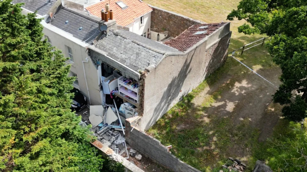 A view of the house from above, showing one outside wall of the property missing with a pile debris on the ground