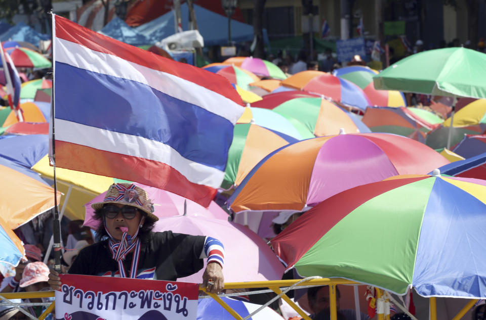 An anti-government protester holds a national flag during a speech from the stage during a rally at the Democracy Monument in Bangkok, Thailand Sunday, Jan. 12, 2014. The protesters want caretaker Prime Minister Yingluck Shinawatra to resign and her government replaced by a non-elected interim administration which will implement reforms they say are needed to stop corruption and money politics. The banner in foreground reads: "Resident of Koh Pa-ngan." (AP Photo/Apichart Weerawong)