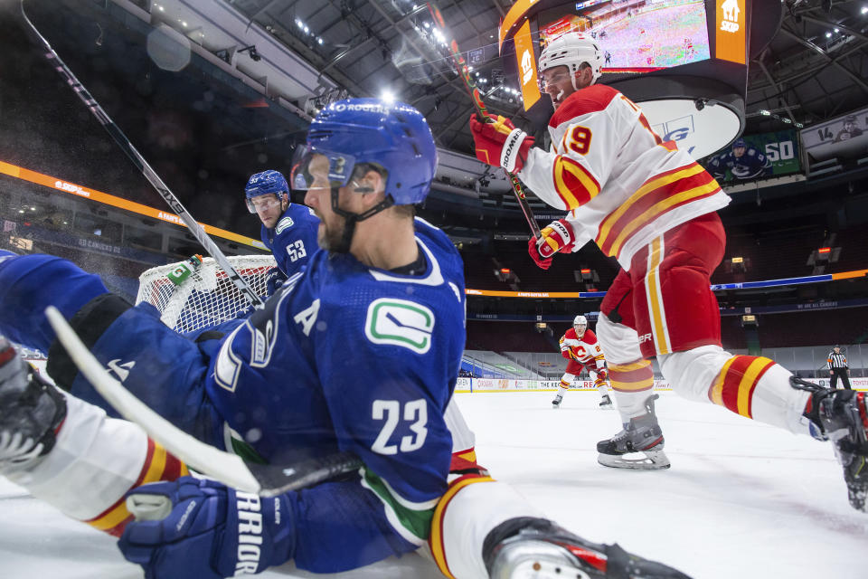 Vancouver Canucks' Alexander Edler (23) falls onto Calgary Flames' Elias Lindholm as Calgary's Matthew Tkachuk (19) and Vancouver's Bo Horvat (53) chase the puck during the second period of an NHL hockey game Saturday, Feb. 13, 2021, in Vancouver, British Columbia. (Darryl Dyck/The Canadian Press via AP)