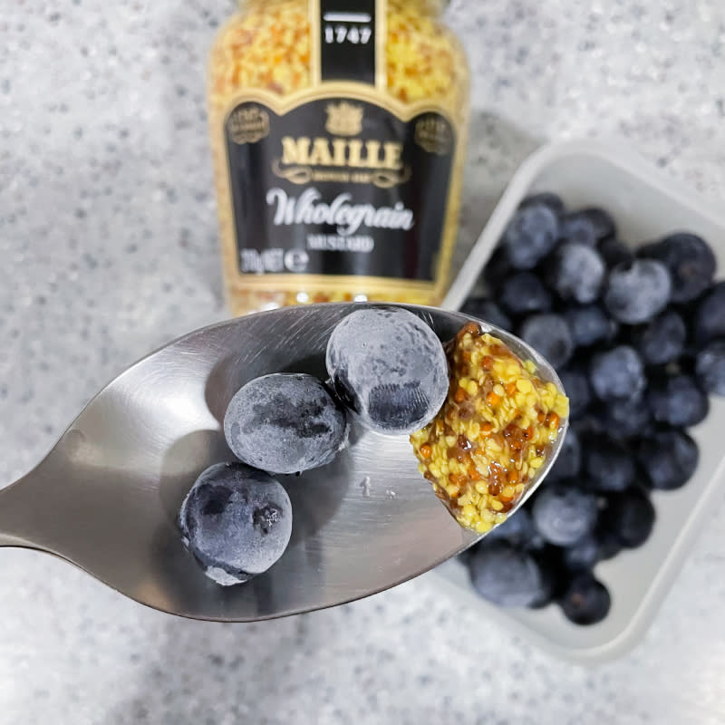 a hand in frame shot of blueberries and mustard