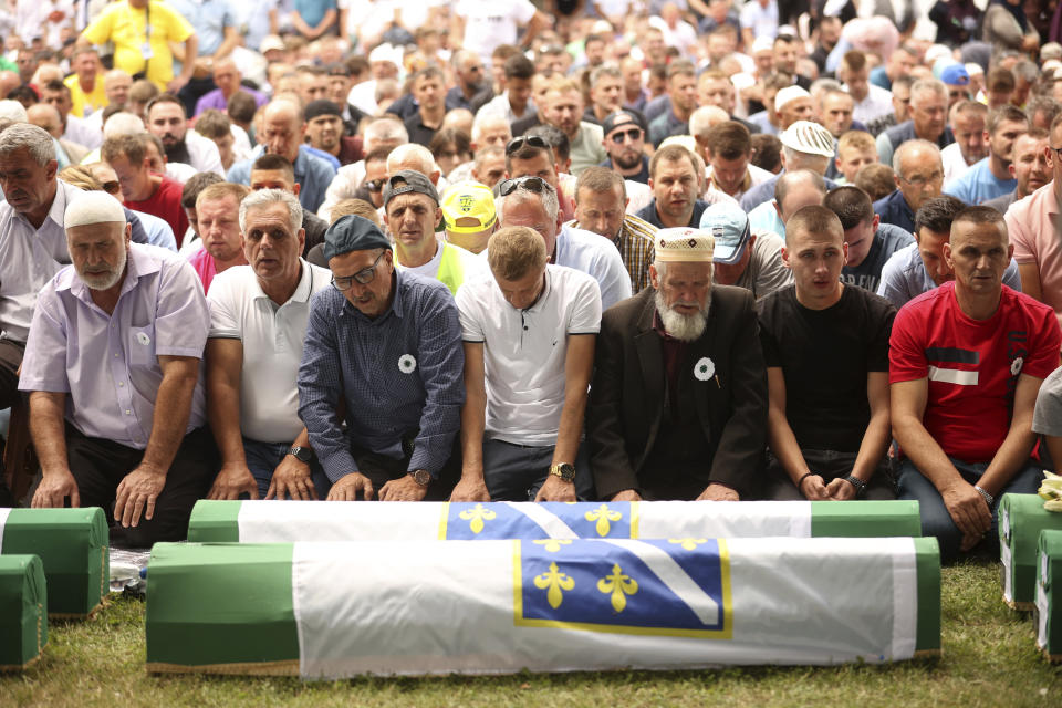 Bosnian muslim men pray next to the coffins containing the remains of 50 newly identified victims of the Srebrenica Genocide, in Potocari, Monday, July 11, 2022. Fifty newly identified victims were honored and reburied Monday in Bosnia as thousands gathered to commemorate the anniversary of the 1995 Srebrenica massacre, Europe’s only acknowledged genocide since the Holocaust. (AP Photo/Armin Durgut)