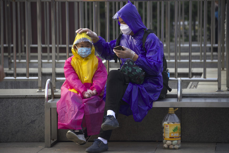 Passengers wearing face masks and raincoats to protect against the spread of new coronavirus sit outside of Hankou train station after of the resumption of train services in Wuhan in central China's Hubei Province, Wednesday, April 8, 2020. After 11 weeks of lockdown, the first train departed Wednesday morning from a re-opened Wuhan, the origin point for the coronavirus pandemic, as residents once again were allowed to travel in and out of the sprawling central Chinese city. (AP Photo/Ng Han Guan)