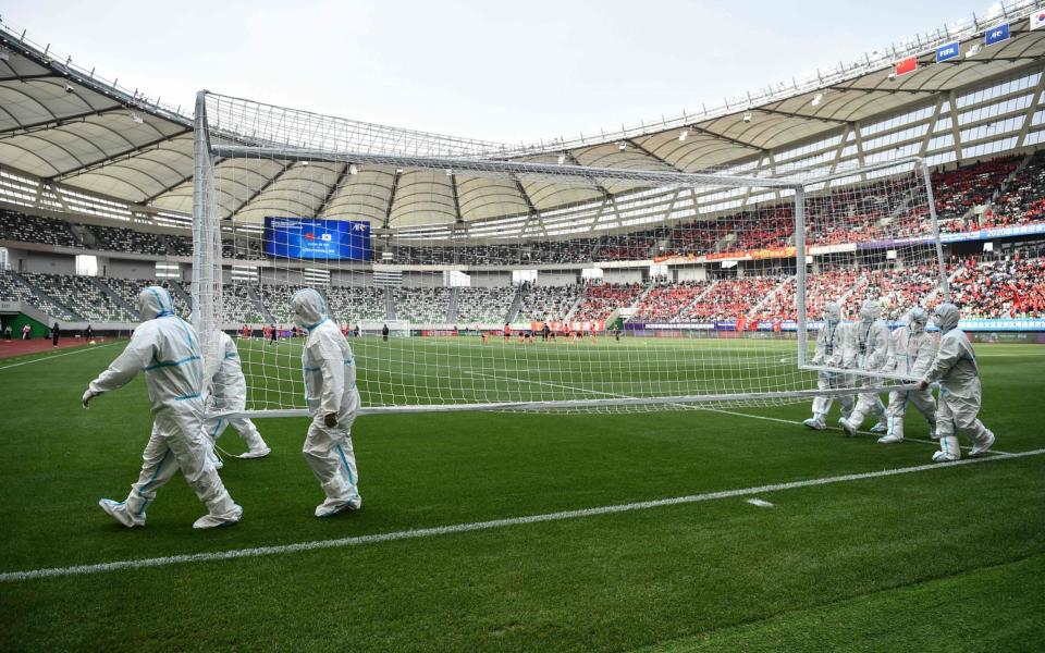 Workers wearing PPE carry a goal post before the qualifying play-off second leg women's football match for the Tokyo 2020 Olympic Games between China and South Korea - HECTOR RETAMAL/AFP 