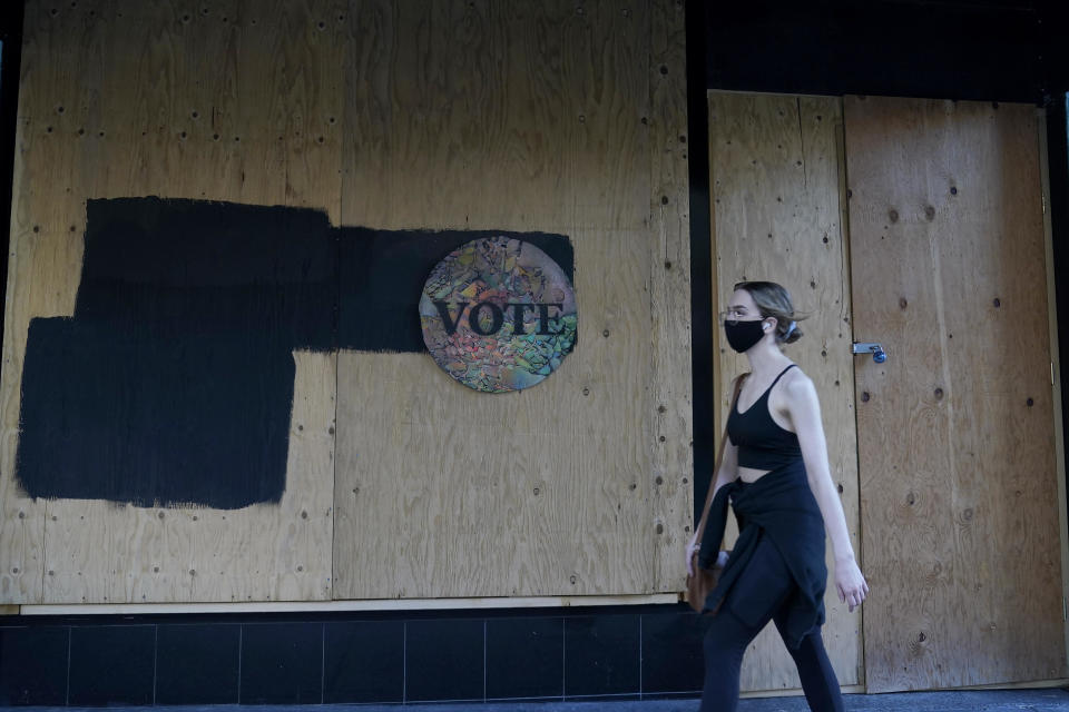 A woman walks past a Vote sign on wooden boards covering the exterior of Chloe Gallery in San Francisco, on Monday, November 2, 2020, ahead of Election Day. / Credit: Jeff Chiu / AP