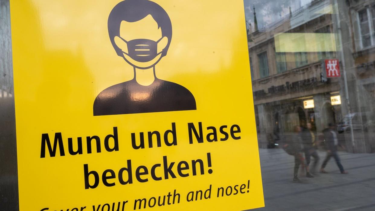 Auf dem Münchener Marienplatz fordert ein Schild zum Tragen eine Mund-Nasen-Bedeckung auf.