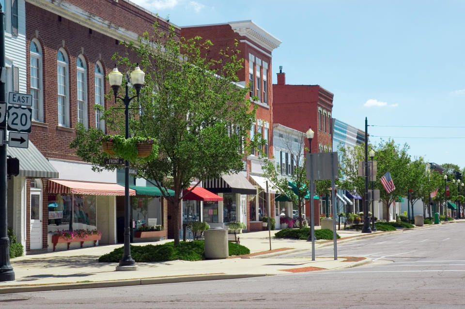 A view of a quaint main street in a small town, with shops lining the road and trees and streetlights dotting the sidewalk