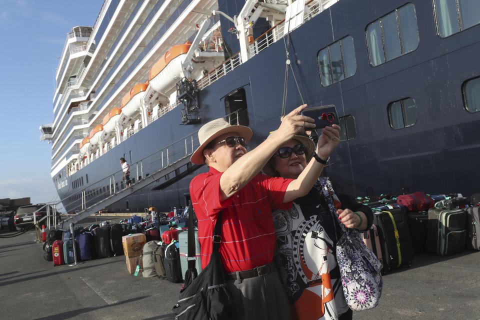 Passengers of the MS Westerdam, owned by Holland America Line, take a selfie after they disembark from the MS Westerdam, back, at the port of Sihanoukville, Cambodia, Saturday, Feb. 15, 2020. After being stranded at sea for two weeks because five ports refused to allow their cruise ship to dock, the passengers of the MS Westerdam were anything but sure their ordeal was finally over. (AP Photo/Heng Sinith)