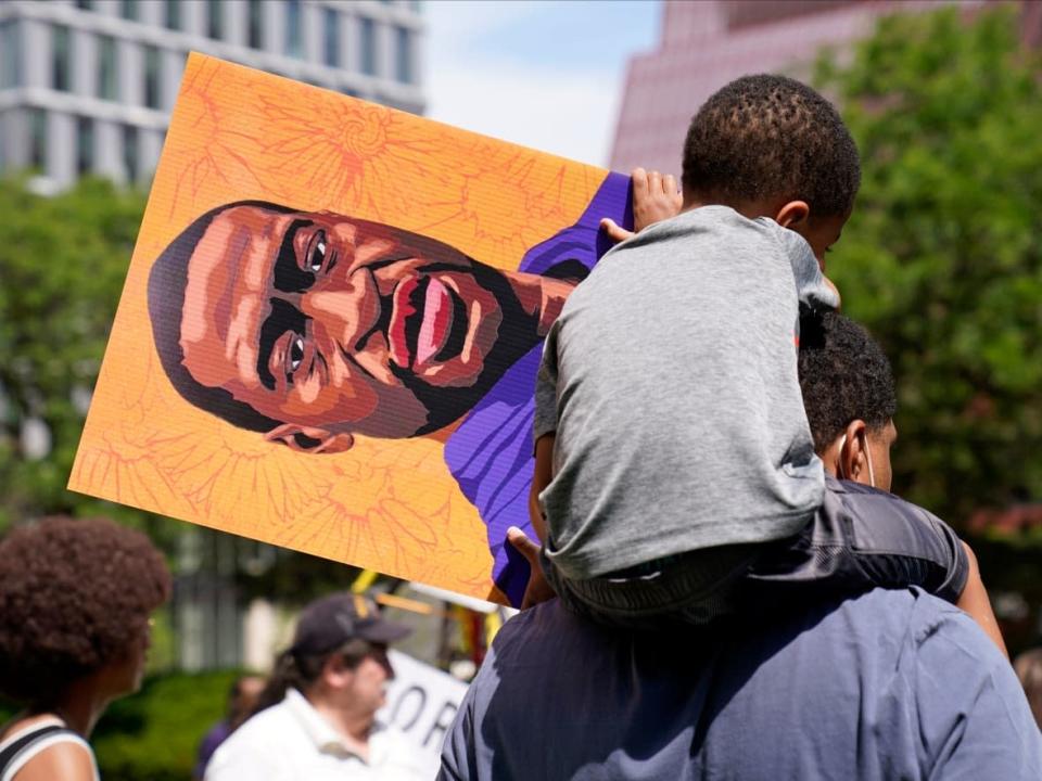 On June 25, 2021 in Minneapolis, a young boy holds a George Floyd poster as he sits on a shoulder after former Minneapolis police officer Derek Chauvin was sentenced to 22-and-a-half years in prison for the May 2020 murder of Floyd. (Jim Mone/The Associated Press - image credit)