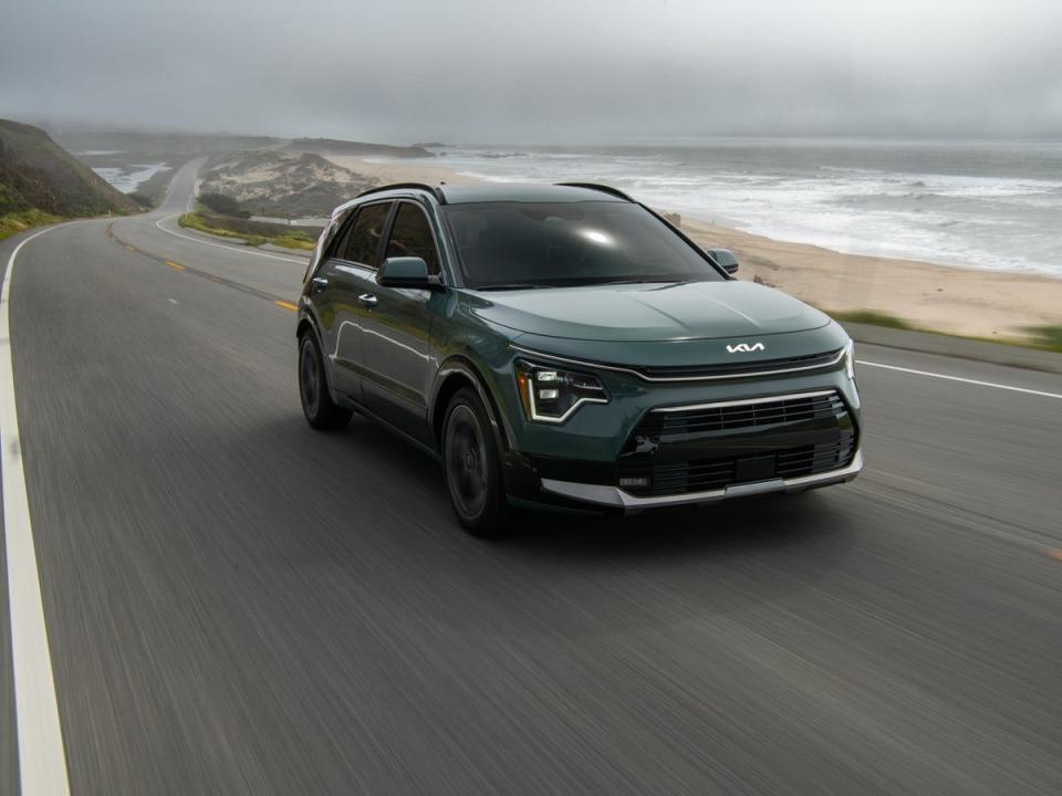 A 2023 Kia Niro drives down a road beside a sandy beach.