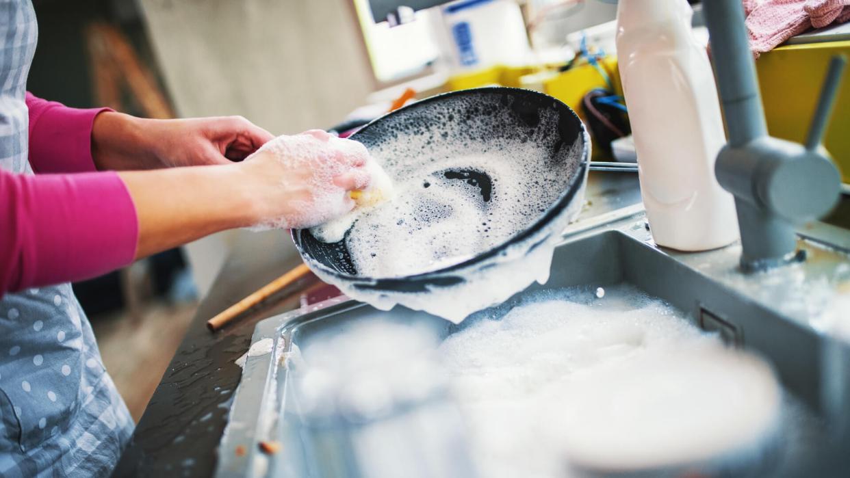 Closeup of unrecognizable woman doing dishes with lots of dirty plates and pots waiting aside.