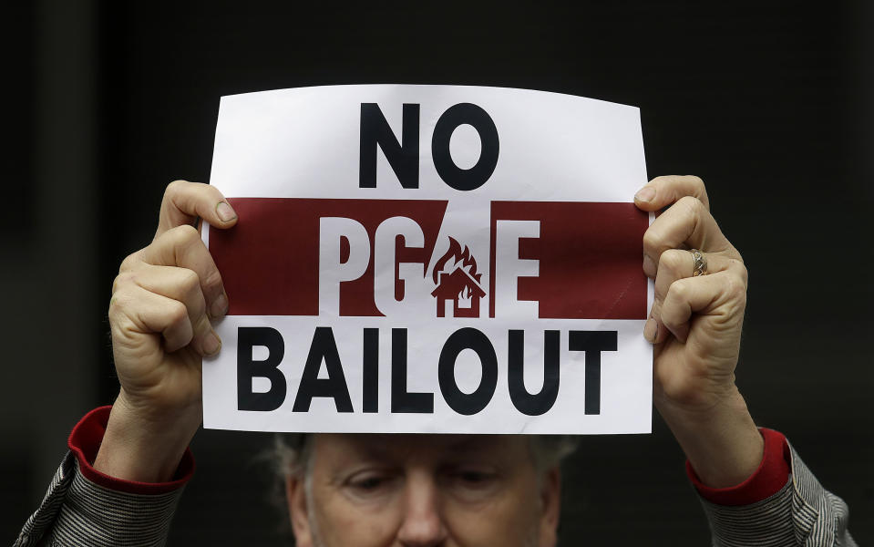 FILE - In this Monday, Jan. 28, 2019 photo, a man holds a sign at a rally before a California Public Utilities Commission meeting in San Francisco. Pacific Gas & Electric has agreed to pay $11 billion to a group of insurance companies representing most of the claims from Northern California wildfires in 2017 and 2018 as the company tries to emerge from bankruptcy, the utility announced Friday, Sept. 13, 2019.(AP Photo/Jeff Chiu, File)