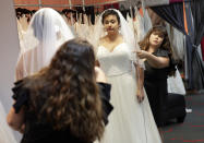 In this Friday, June 21, 2019, photo Ann Campeau,, right, owner of Strut Bridal, fits a new dress on inventory manager Stefanie Zuniga at her shop in Tempe, Ariz. Cut-rate prices on websites that sell wedding dresses direct from China put pressure on Campeau, who owns four bridal shops in California and Arizona. She has had customers come in after seeing low-end gowns online and expecting to get a dress at a similar price. (AP Photo/Matt York)