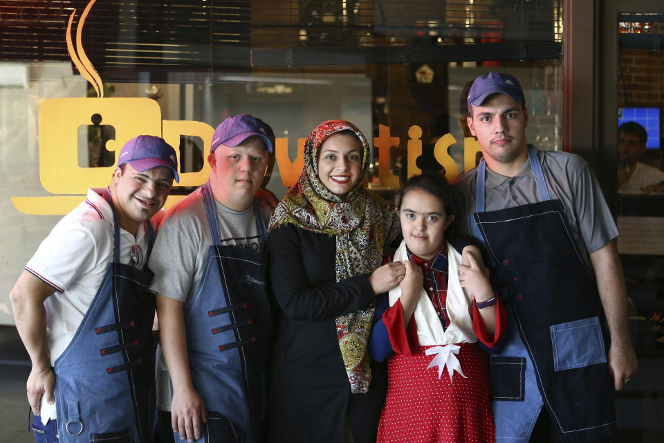 In this Monday, Aug. 6, 2018, photo, Aylin Agahi founder of Downtism Cafe and a musician, center, poses for a photo with some of her staff, in Tehran, Iran. The popular cafe in Tehran’s bustling Vanak Square, whose name combines “Down” with “autism,” is entirely run by people with Down syndrome or autism. More than just providing meaningful work, the cafe is helping break down barriers by highlighting how capable people with disabilities are. (AP Photo/Ebrahim Noroozi)