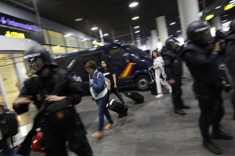 Passengers walk past a line of riot police standing on the way of protestors outside El Prat airport in Barcelona, Spain, Monday, Oct. 14, 2019. Spain's Supreme Court on Monday convicted 12 former Catalan politicians and activists for their roles in a secession bid in 2017, a ruling that immediately inflamed independence supporters in the wealthy northeastern region. (AP Photo/Emilio Morenatti)