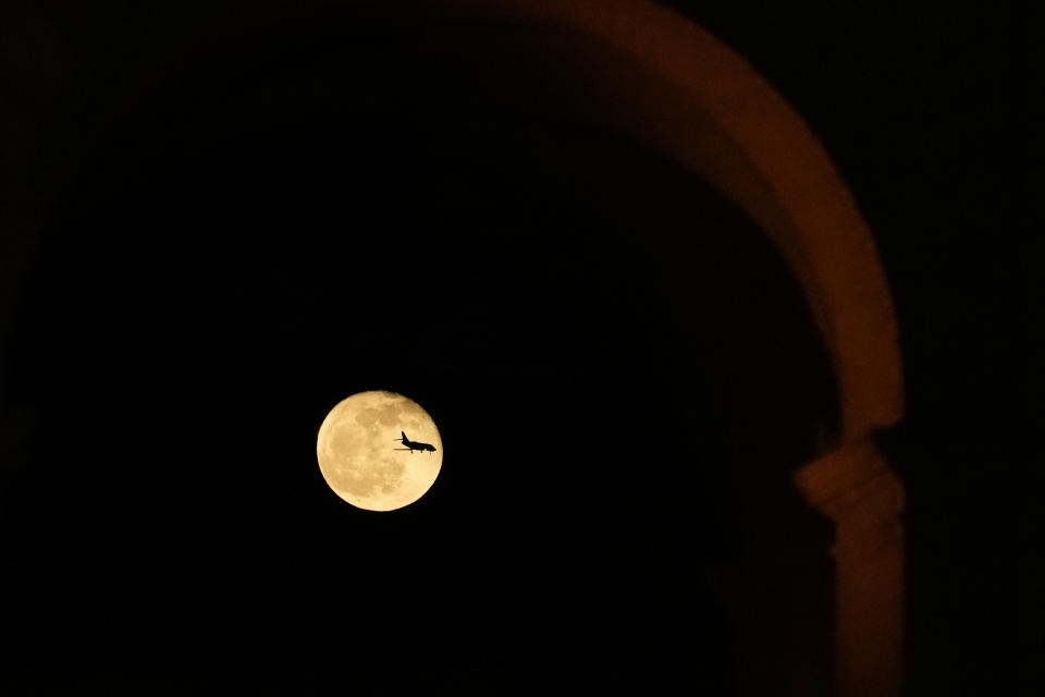 An airplane passes if front of the moon as it shines over the Colosseum during a Via Crucis (Way of the Cross) torchlight procession on Good Friday, in Rome, Friday, April 7, 2023. The Vatican says Pope Francis won't go to the Colosseum for the traditional Good Friday procession but instead he will watch it from his home at the Vatican due to unseasonably cold nighttime temperatures in Rome. (AP Photo/Alessandra Tarantino)