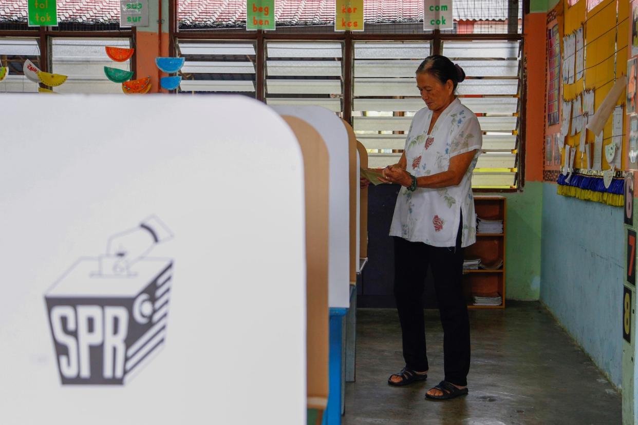 An elderly woman in white casting her vote at a voting centre in Malaysia.