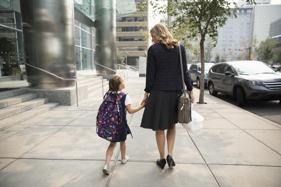 Businesswoman mother and schoolgirl daughter walking on urban sidewalk