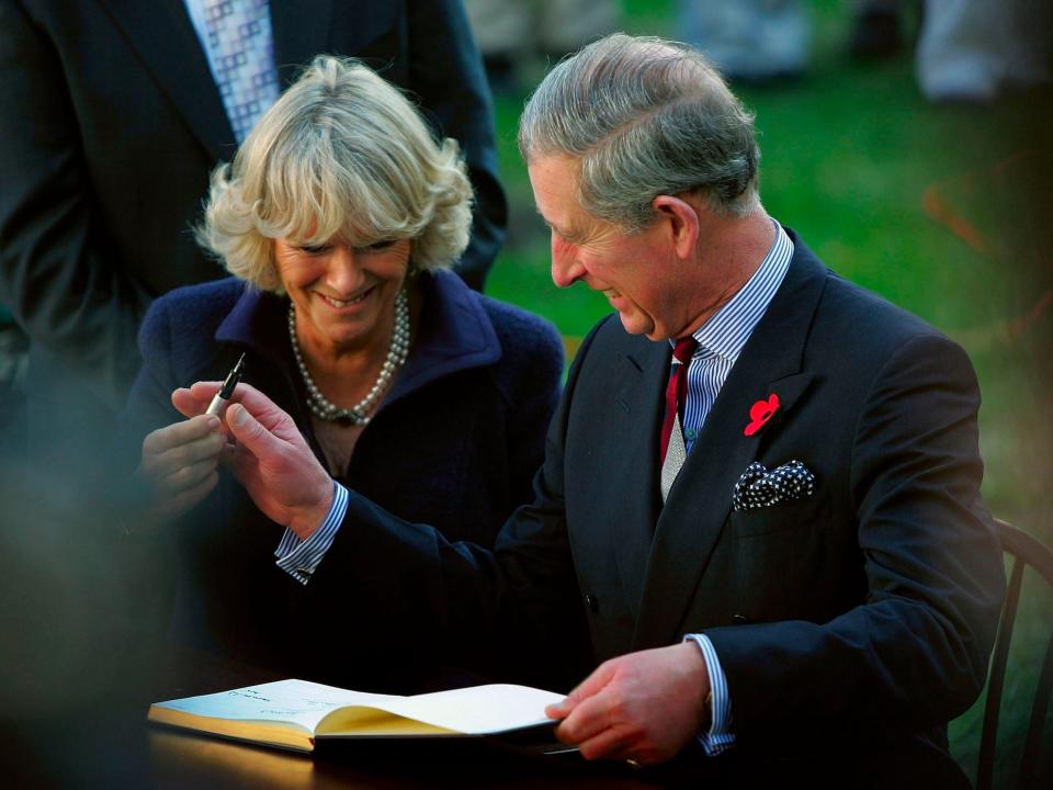 Camilla, Queen Consort and King Charles III laugh as he passes a pen to her.