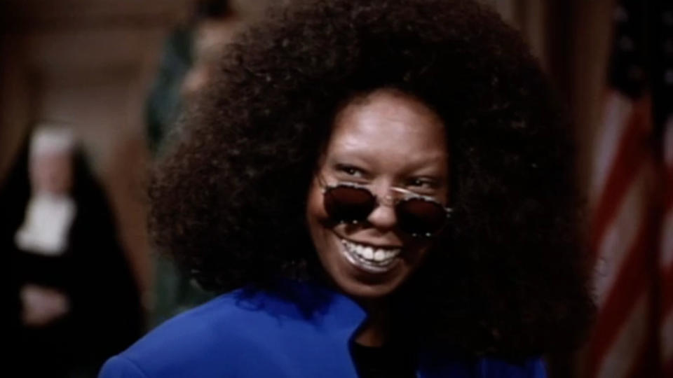 Whoopi Goldberg smiles while wearing sunglasses and a blue jacket in Sister Act 2.
