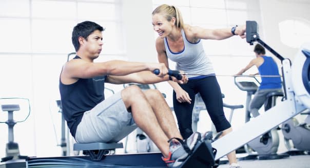 Personal trainer with man on rowing machine in gymnasium