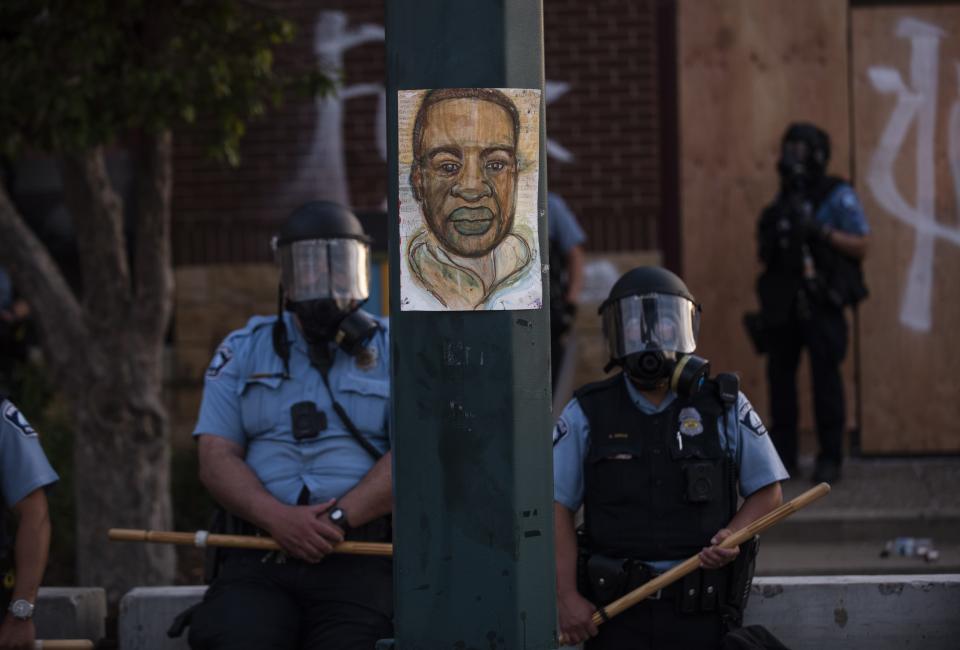 A portrait of George Floyd hangs on a street light pole as police officers stand guard at the Third Police Precinct during a face-off with a group of protesters on May 27, 2020, in Minneapolis.