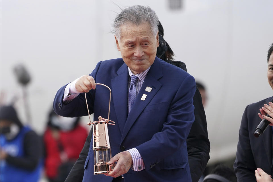 FILE - In this March 20, 2020, file photo, Tokyo 2020 Olympics chief Yoshiro Mori carries the Olympic flame during the Flame Arrival Ceremony at Japan Air Self-Defense Force Matsushima Base in Higashimatsushima in Miyagi Prefecture, north of Tokyo. Tokyo Olympic organizers seem to be leaning away from starting the rescheduled games in the spring of 2021. More and more the signs point toward the summer of 2021. Organizing committee President Mori suggested there would be no major change from 2020. (AP Photo/Eugene Hoshiko, File)