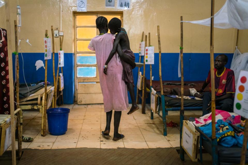 A women, facing away, holds a sick child in a hospital room.