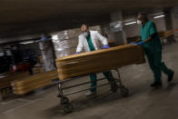 workers move a coffin with the body of a victim of coronavirus as others coffins are stored waiting for burial or cremation at the Collserola morgue in Barcelona, Spain, Thursday, April 2, 2020. The new coronavirus causes mild or moderate symptoms for most people, but for some, especially older adults and people with existing health problems, it can cause more severe illness or death. (AP Photo/Emilio Morenatti)