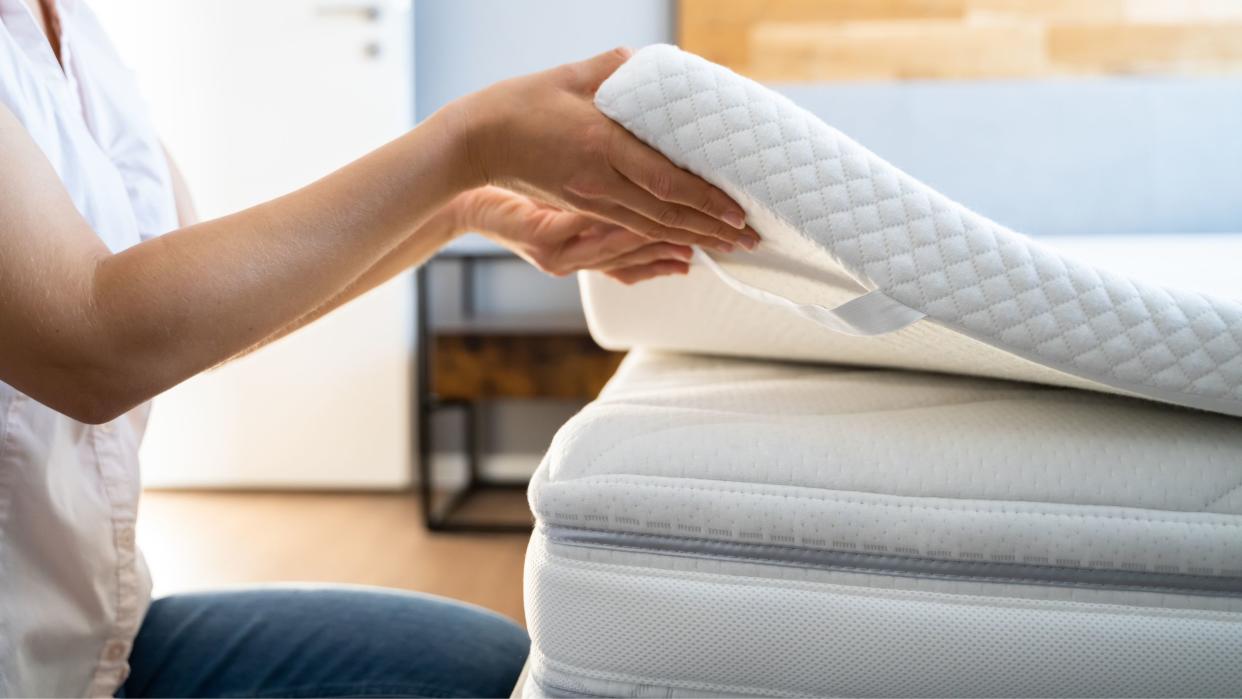  How to keep a mattress topper from sliding: Mattress topper on mattress with lady holding the corner over the bed 