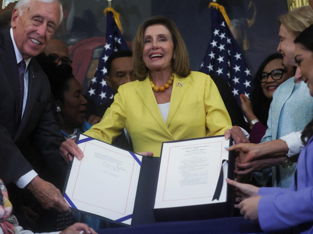 nancy pelosi holds up signed bill surrounded by congress representatives