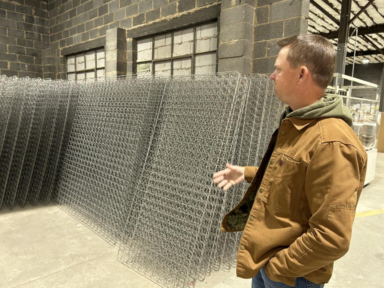 Justin Faison, owner and CEO of Winndom Mattress, looks over the coil-spring frames that line a wall of the company's new manufacturing facility on Randolph Road in Hopewell on Wednesday, Dec. 13, 2023. A fire earlier this year destroyed the company's location on Rev. CW Harris Street, but Faison said within six weeks, custom mattress orders were filled.